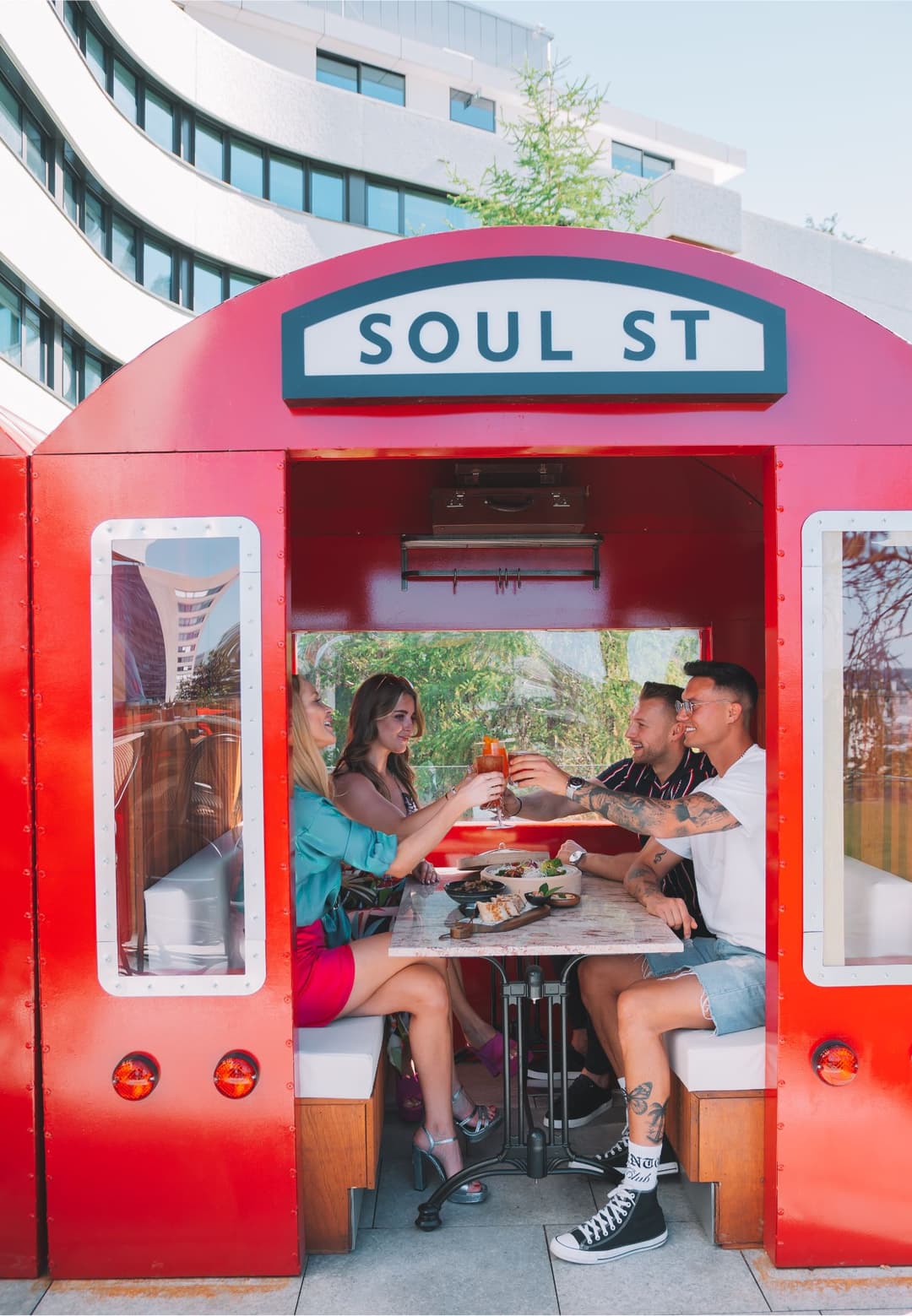 Trois personnes trinquent avec des cocktails à l'intérieur d'un food truck rouge vif Soul St, avec des assiettes de street food sur la table