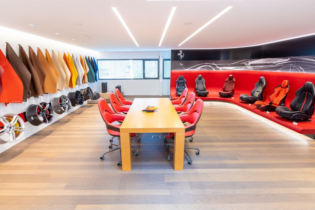 Espace de configuration Ferrari avec table de réunion en bois, sièges rouges, palette de couleurs de carrosserie et sièges d'intérieur exposés