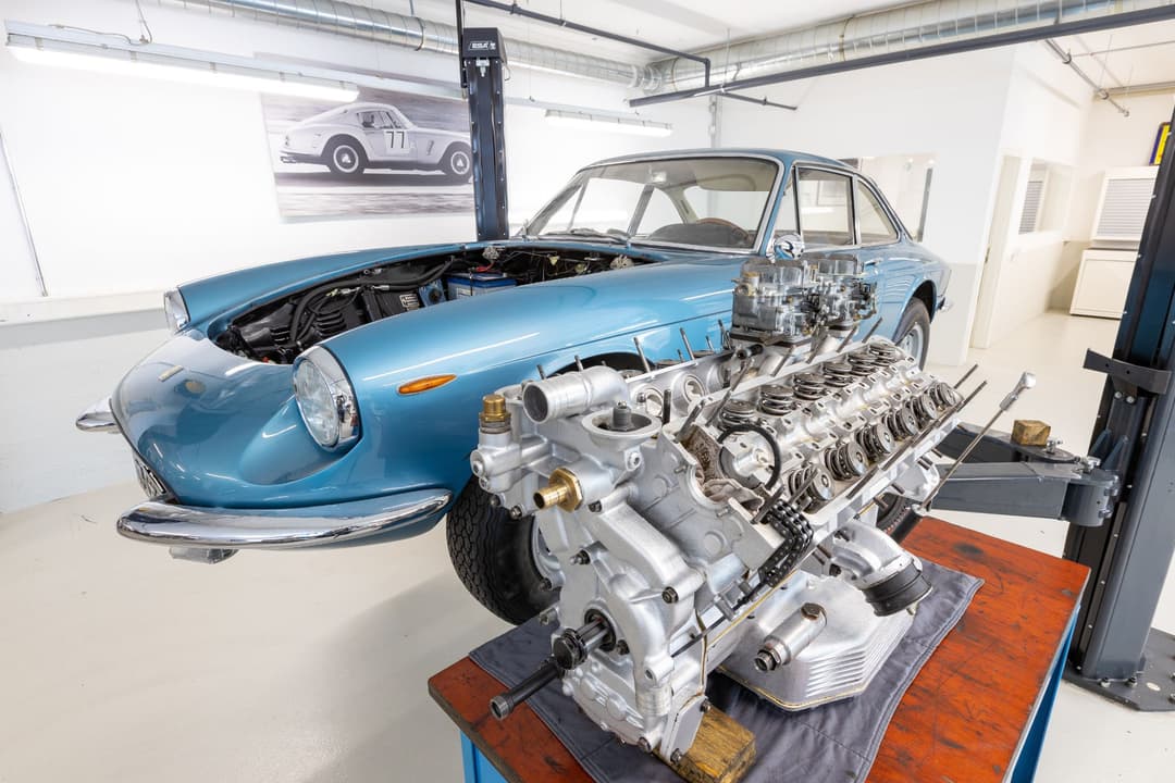 Ferrari bleue avec capot ouvert et moteur V12 détaché exposé à l'atelier Modena Cars de Genève