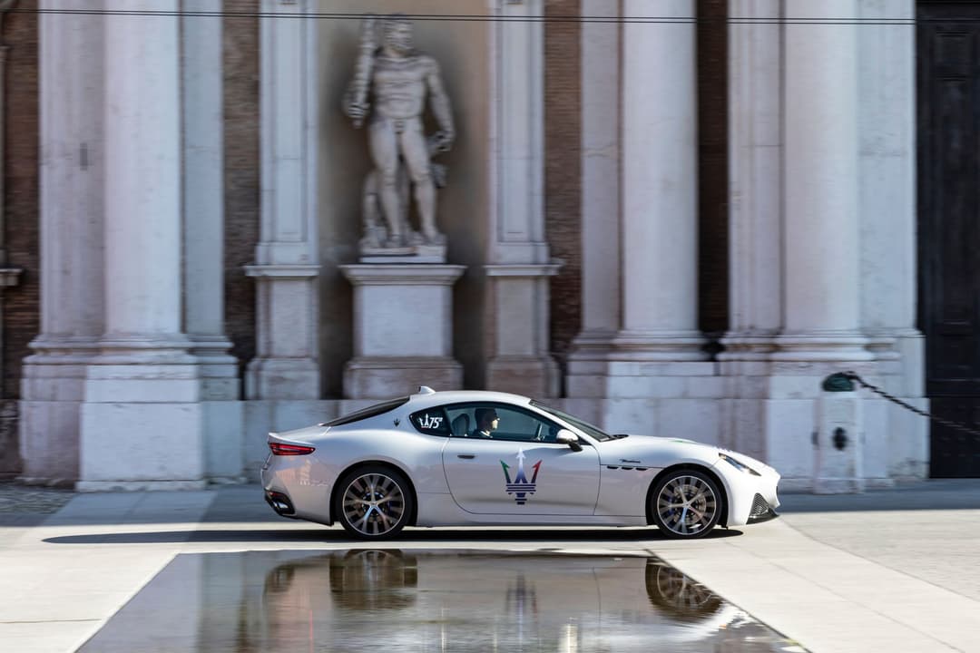 Maserati GranTurismo blanche avec le trident au flanc, garée devant une façade classique avec colonnes et statue