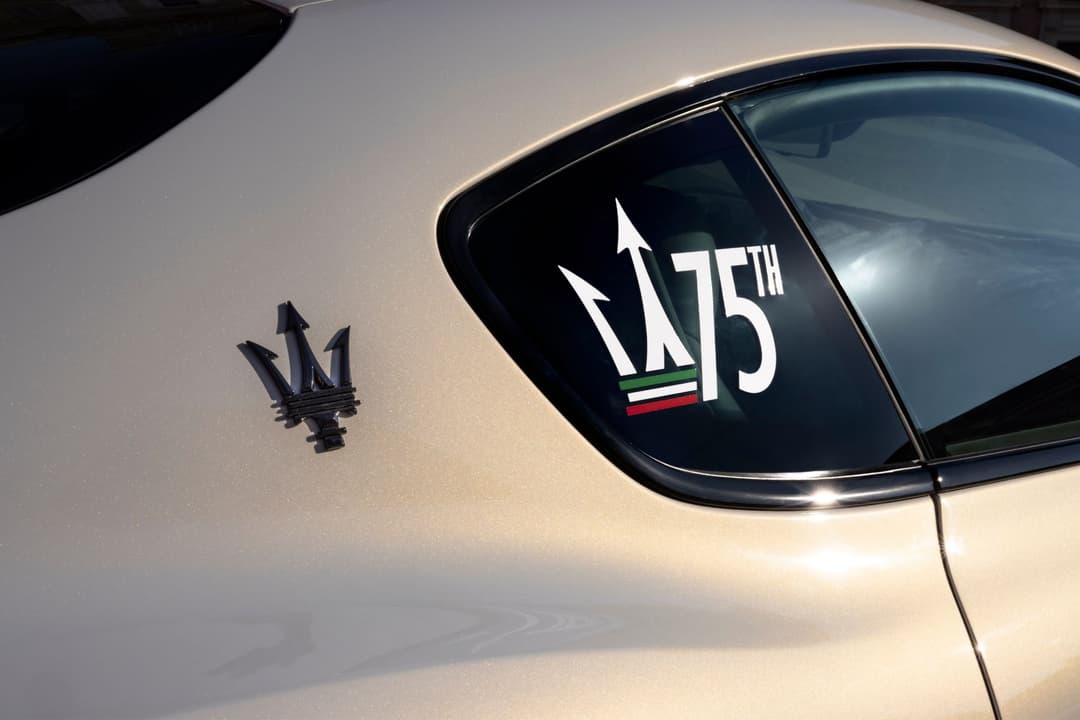 Détail d'une Maserati GranTurismo beige avec le logo du trident sur la portière et un autocollant commémoratif 175th anniversary sur la vitre arrière