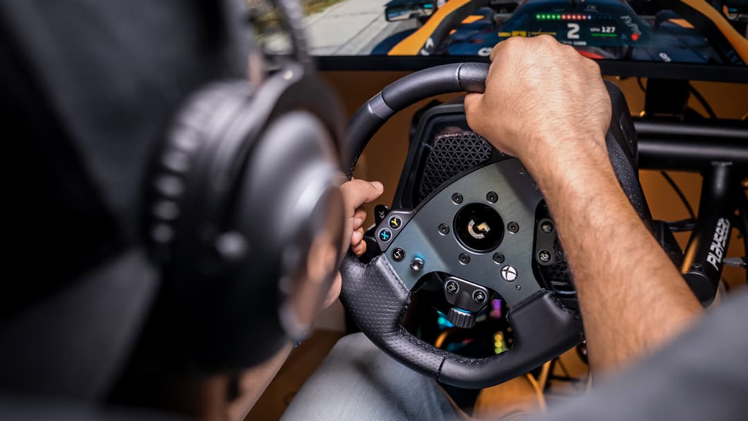 Volant de course Logitech G PRO Racing noir tenu par un joueur, avec écran de jeu en arrière-plan