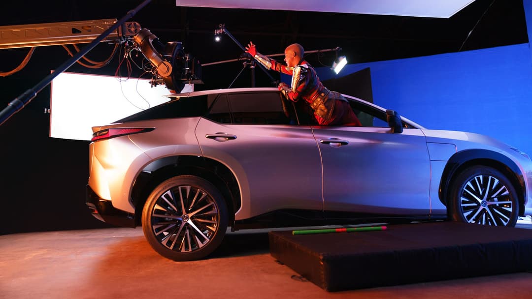 Lexus RZ 450e aux couleurs dégradées bleu et rose, entouré de guerrières Dora Milaje en costumes rouges et or sur un plateau de tournage
