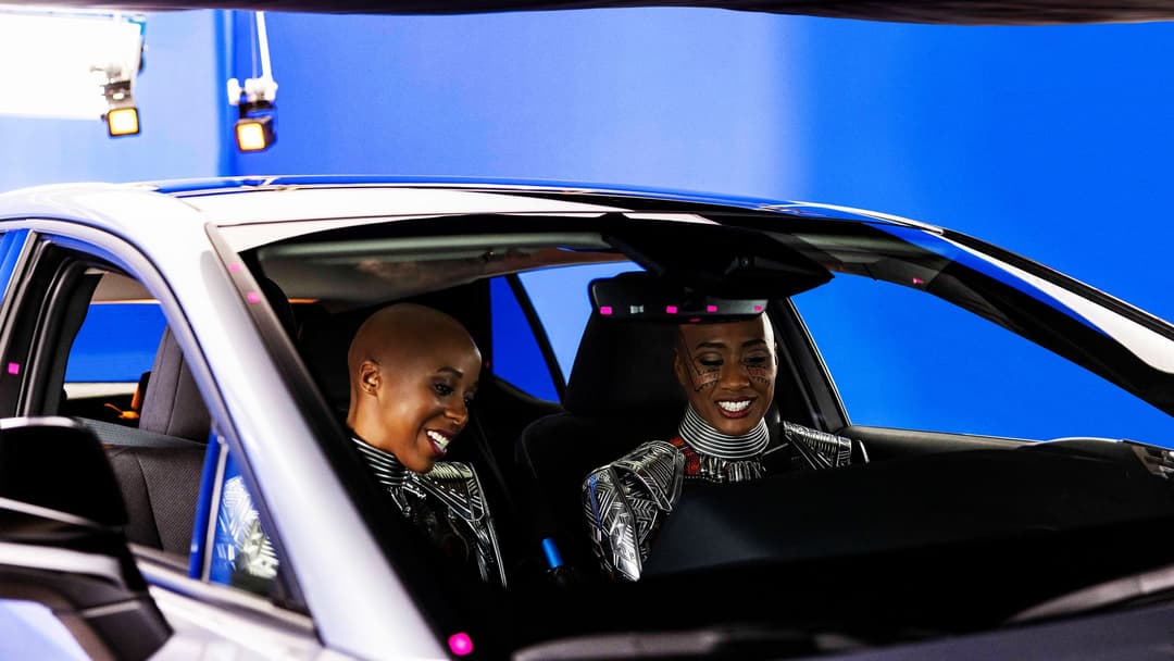 Lexus RZ 450e bleu et blanc avec deux femmes souriantes en tenue Wakanda à l'intérieur