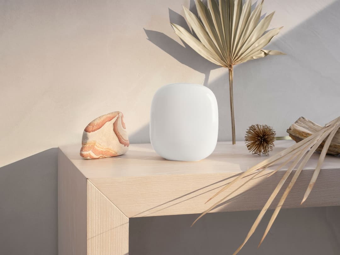 Google Nest Wifi Pro blanc posé sur un meuble clair aux côtés d'éléments de décoration naturels