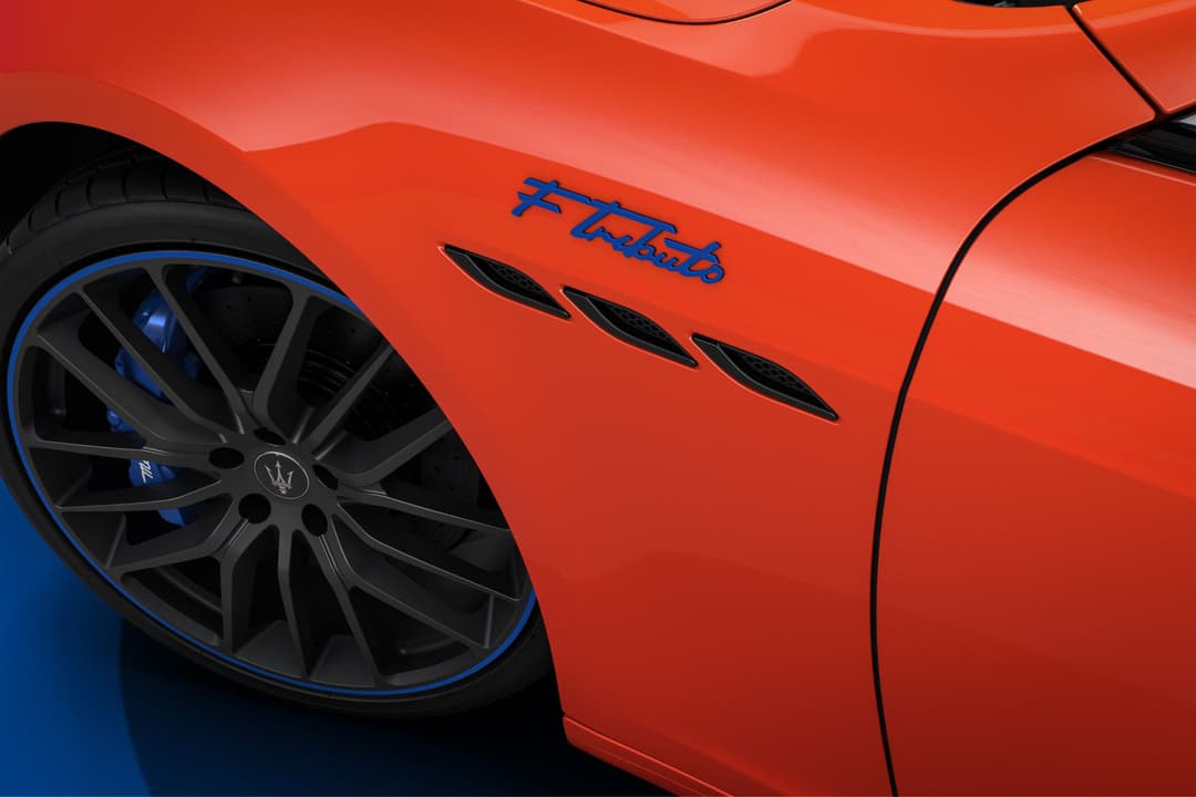 Détail du flanc d'une Maserati Levante rouge Arancio Devil avec badge FTributo bleu, jante noire à liseré bleu cobalt et logo Trident
