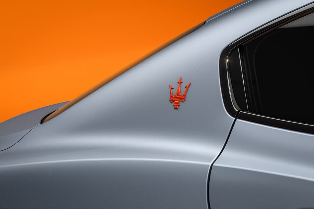 Maserati Ghibli FTributo gris clair avec logo Trident orange sur le pilier C, fond orange