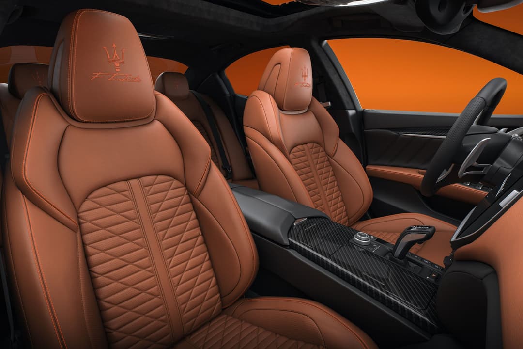 Intérieur de Maserati avec sièges en cuir cognac ornés du logo de la marque et détails orange, volant noir et finitions sportives