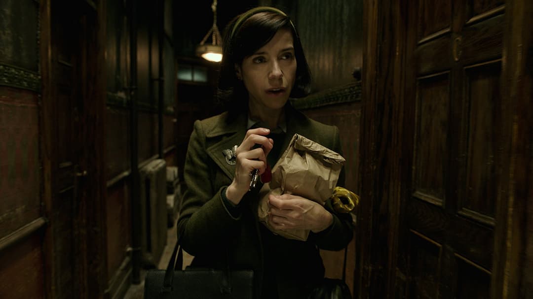 Sally Hawkins dans un couloir sombre tenant une clé, vêtue d'un manteau kaki, scène du film The Shape of Water