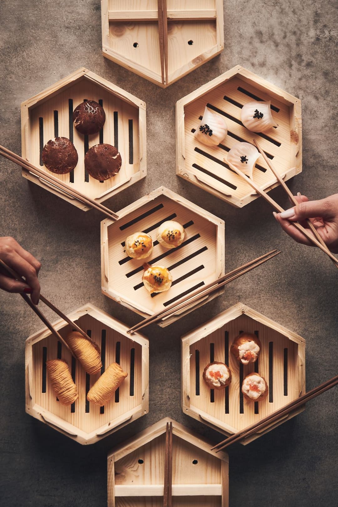 Paniers en bambou hexagonaux contenant différents dim sum et plats chinois, avec des baguettes en bois, vue de dessus sur fond gris