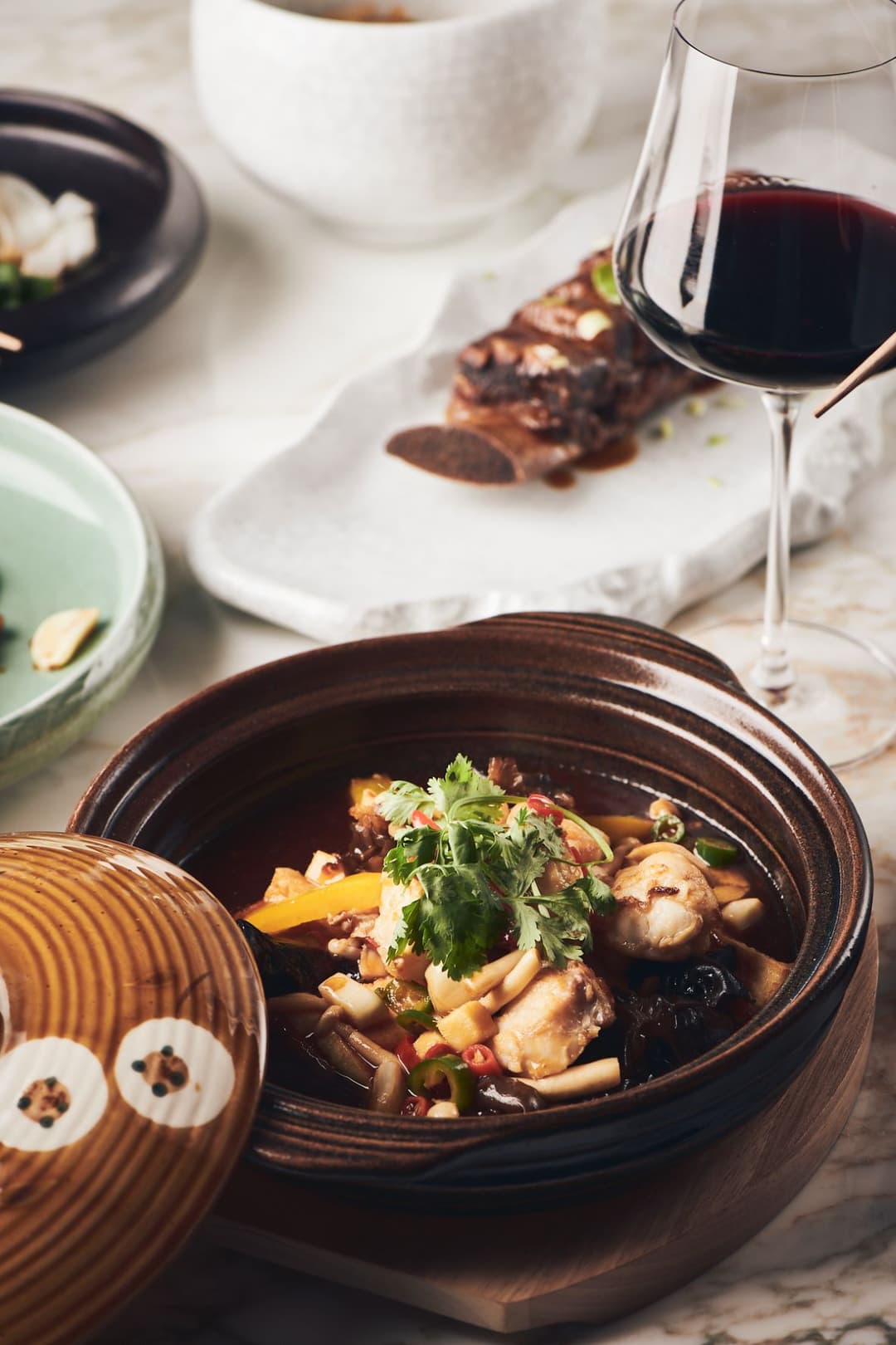 Plat chinois en cocotte brune garni de fruits de mer et légumes frais, accompagné de verre de vin rouge et vaisselle blanche