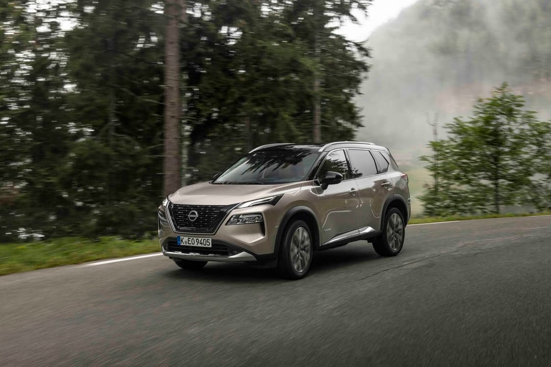 Nissan X-Trail beige en mouvement sur une route forestière entourée de sapin et de végétation