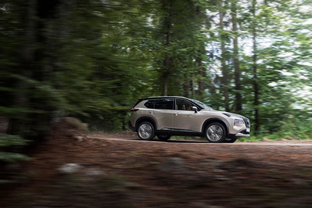 Nissan X-Trail blanc roulant sur un chemin forestier bordé d'arbres verts