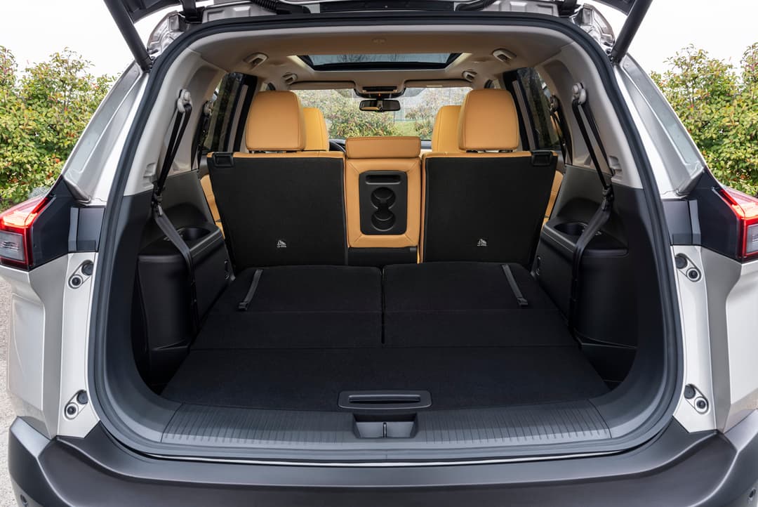 Nissan X-Trail avec hayon ouvert montrant le coffre spacieux modulable aux sièges repliés et intérieur aux sièges orange et noirs