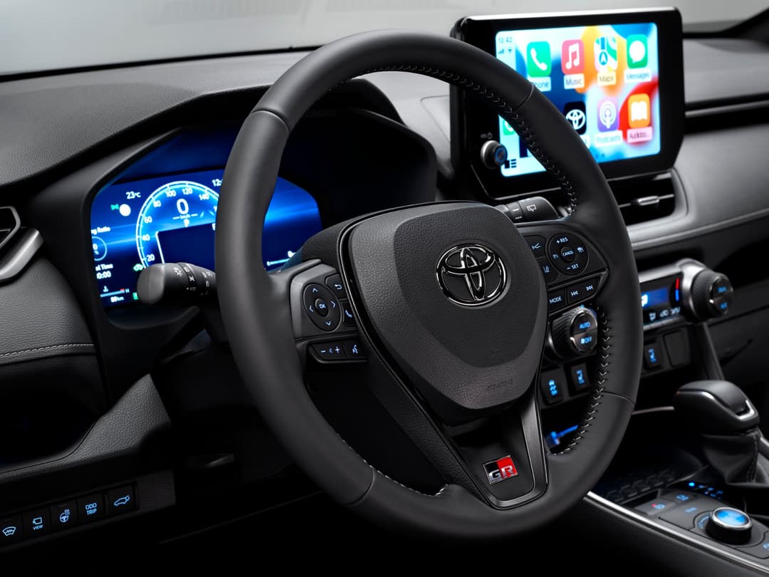 Intérieur du Toyota RAV4 GR SPORT avec volant noir, écrans numériques bleus et écran tactile coloré affichant des applications