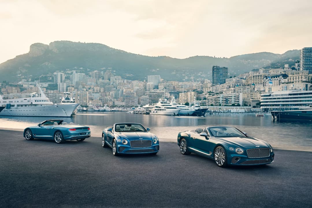 Trois Bentley de la collection Riviera en bleu Aegean, exposées sur un quai face à des yachts et aux montagnes côtières