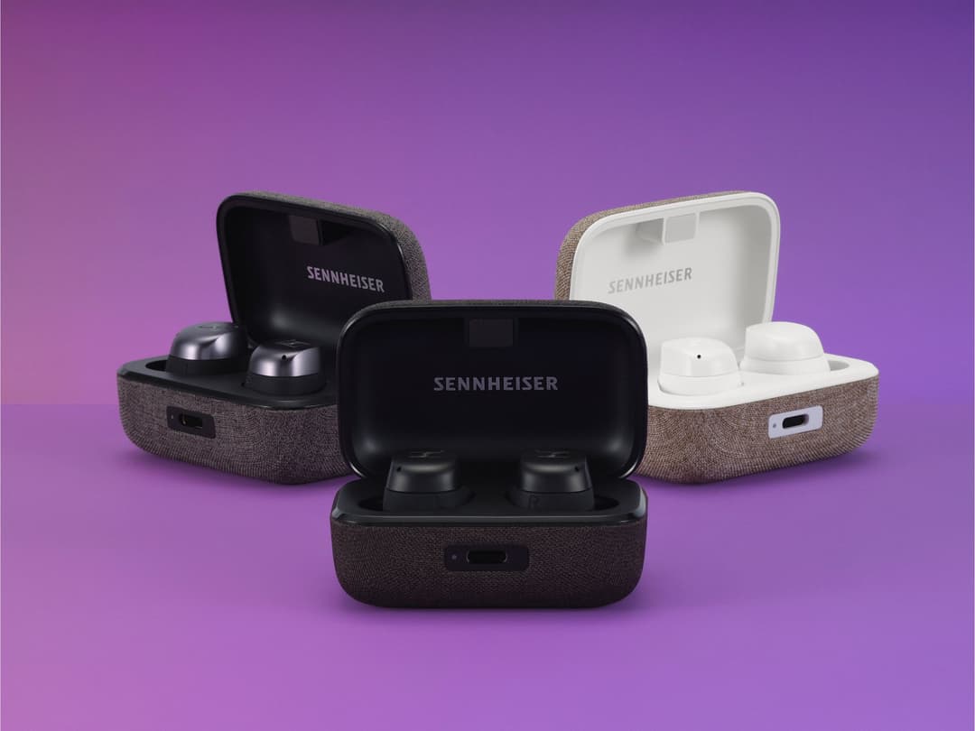 Trois étuis de écouteurs sans fil Sennheiser MOMENTUM 4 de couleurs différentes, ouverts, sur fond violet