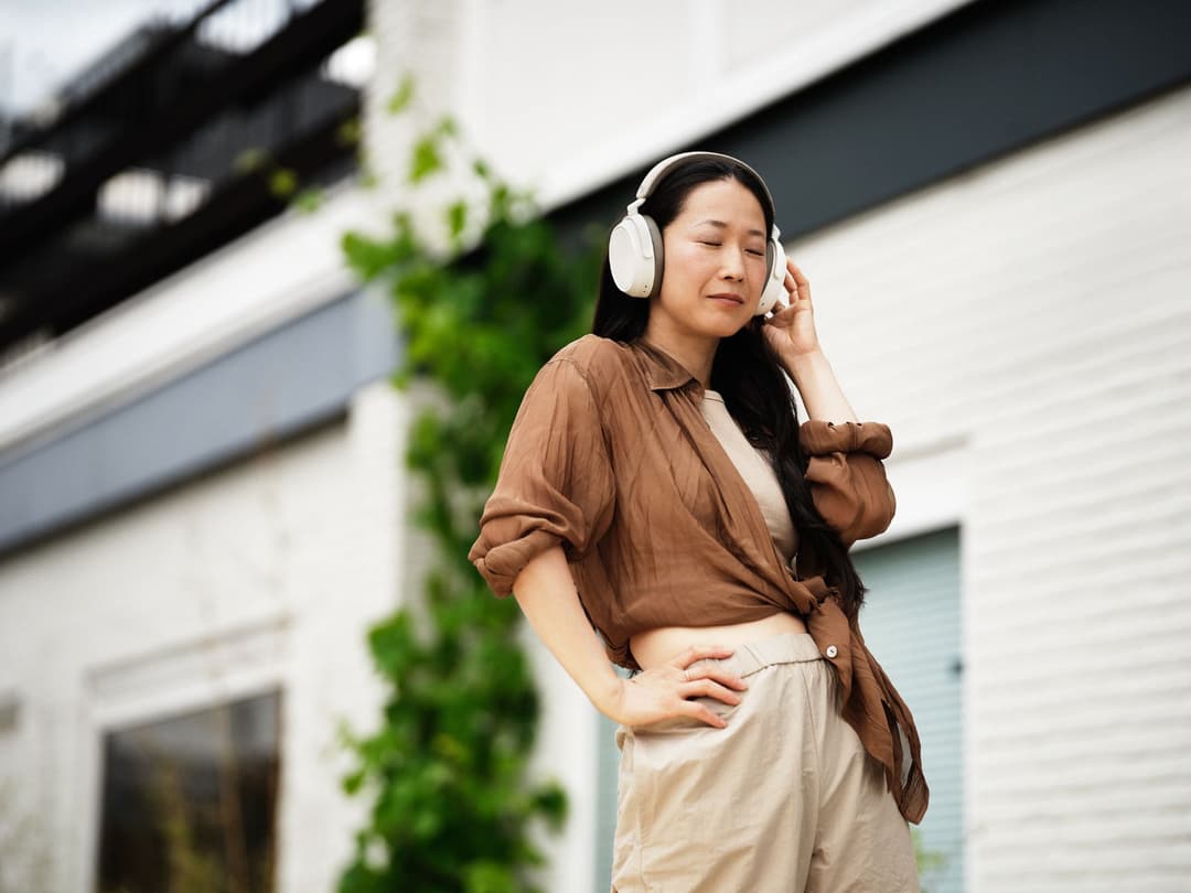 Femme portant un casque Sennheiser MOMENTUM True Wireless 3 blanc, ajustant l'écouteur, vêtue d'une chemise marron