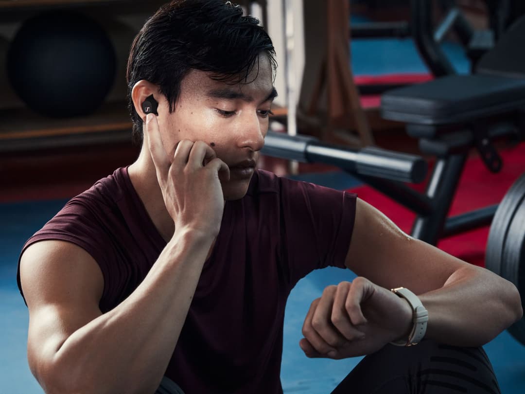 Homme portant des écouteurs Sennheiser noirs, consultant sa montre dans une salle de sport