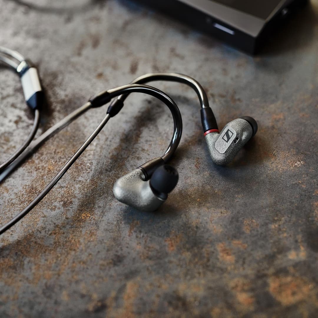 Écouteurs intra-auriculaires Sennheiser gris et noirs avec câble, posés sur une surface texturée