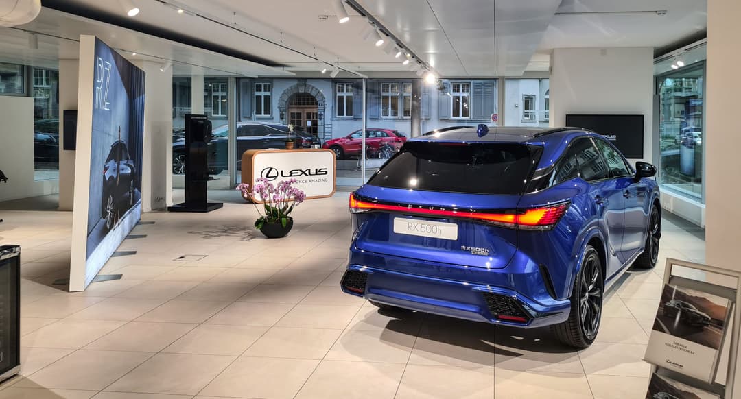 Lexus RX bleu présenté dans le Lexus City Store de Zurich, avec signalétique de marque et autres véhicules visibles en arrière-plan