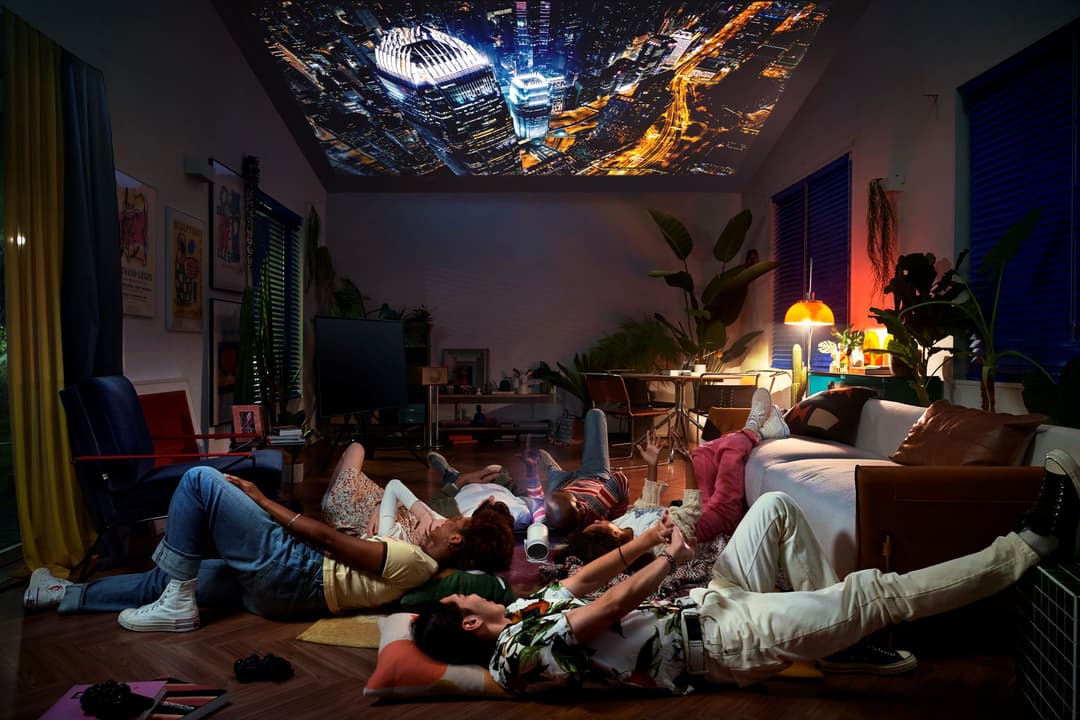 Groupe de personnes allongées sur le sol d'un salon moderne regardant une projection aérienne de ville illuminée au plafond