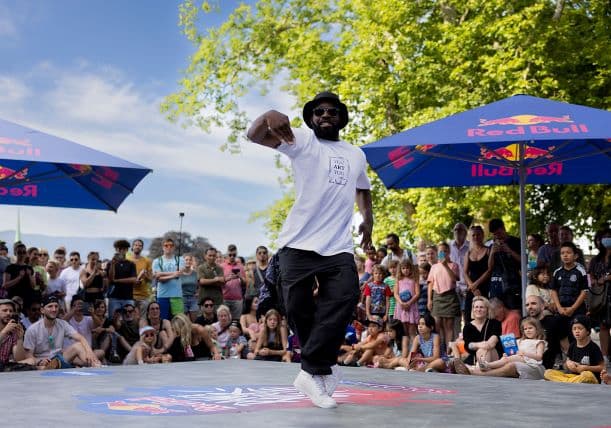 Danseur de hip-hop en train de performer sur une piste devant un public, sous des parasols Red Bull, par beau temps