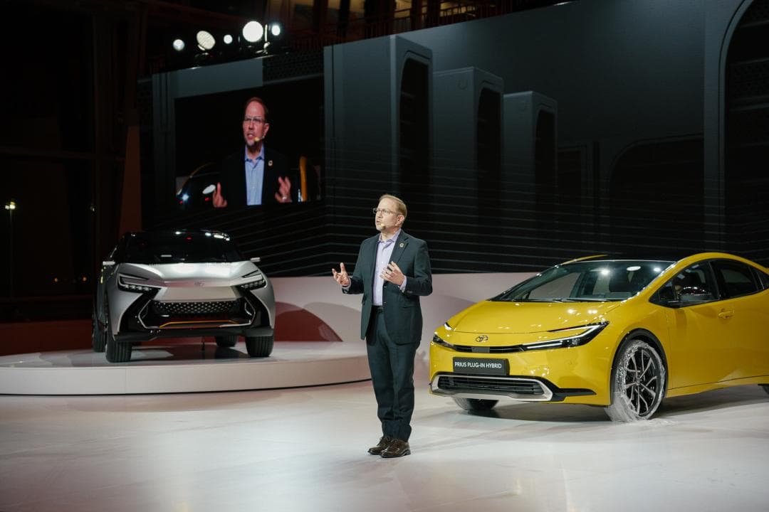 Dr James Kuffner présente les stratégies logicielles de Toyota, entouré d'un véhicule électrique blanc et d'une Prius jaune hybride rechargeable