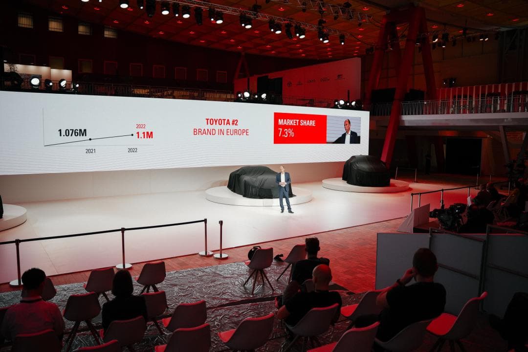 Matt Harrison, président et CEO de Toyota Motor Europe, sur scène lors d'une présentation devant un écran affichant les chiffres de vente et la part de marché de la marque