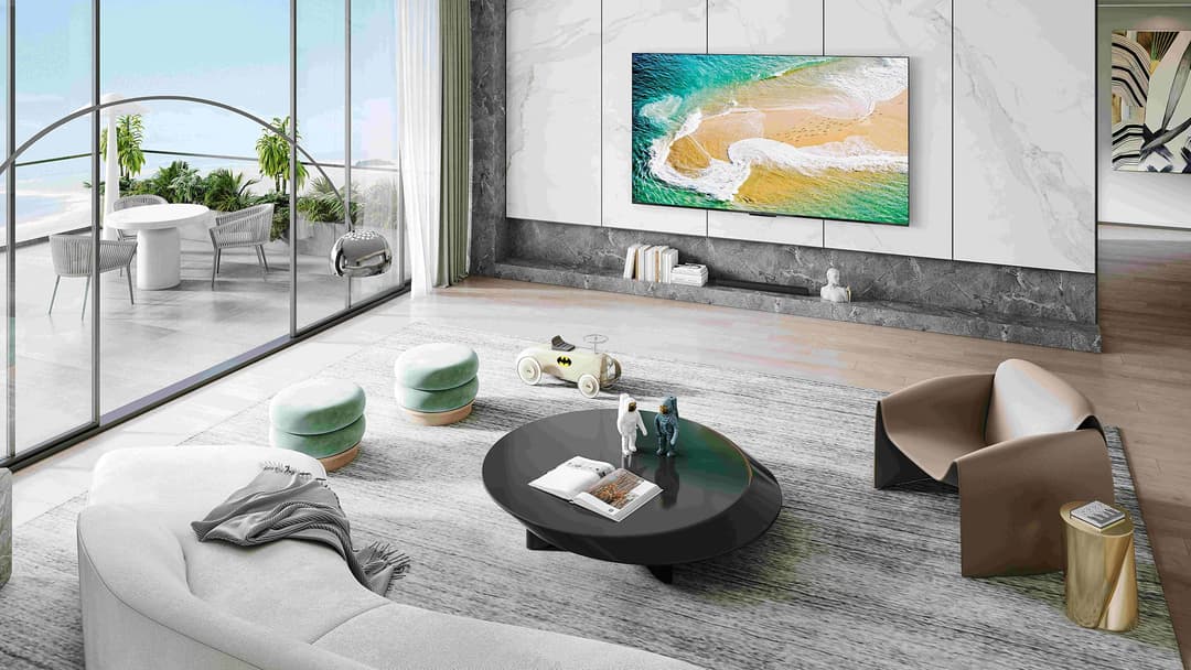 Téléviseur TCL C83 Series affichant une vue aérienne de plage avec vagues turquoise, fixé au mur d'un salon moderne aux tons clairs