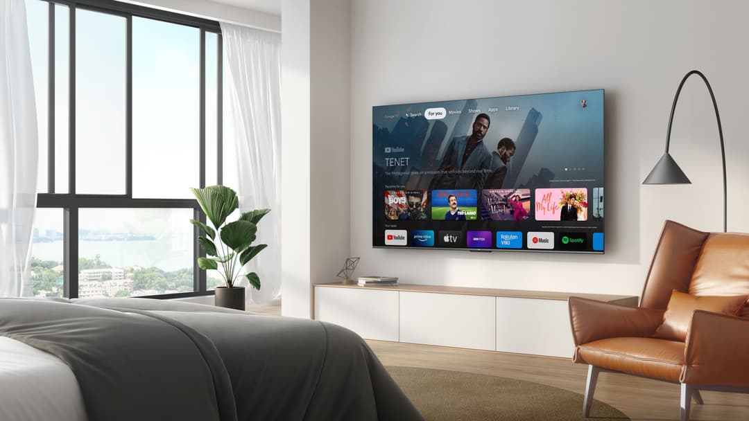 Téléviseur TCL P73 Series affichant l'interface Google TV dans un salon moderne avec fauteuil en cuir et vue sur la ville