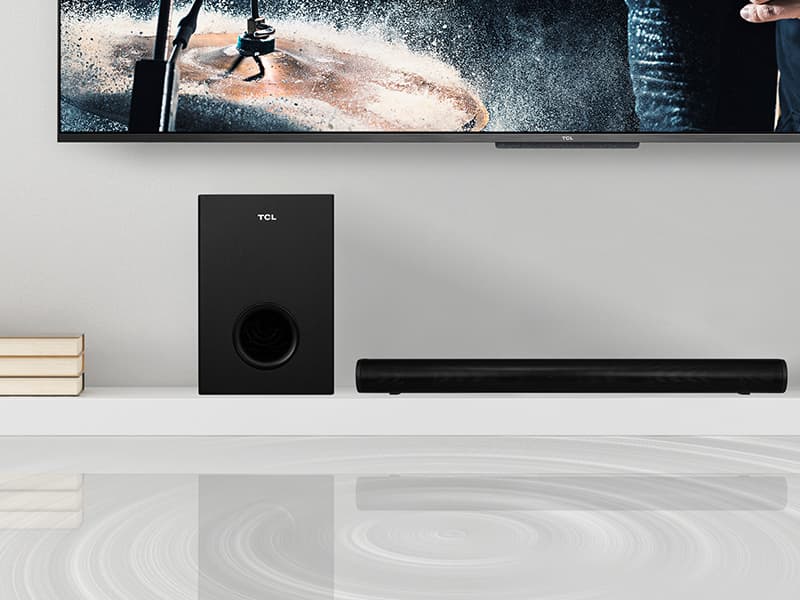 Barre de son TCL S522W noire avec caisson de basses, positionnée sous un téléviseur affichant une scène d'action