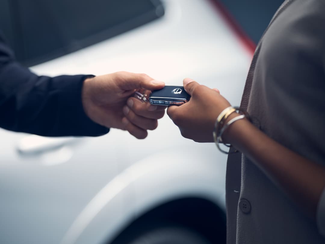 Deux mains échangent une clé de voiture Volvo avec un véhicule blanc en arrière-plan
