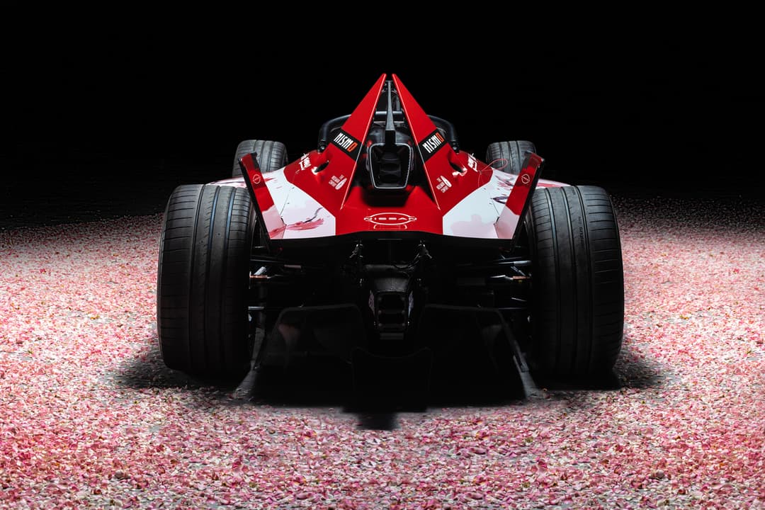 Monoplace Nissan Formula E rouge et blanche vue de l'arrière, sur un sol de graviers roses, fond noir