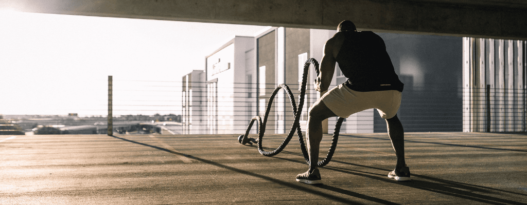 Homme en tenue de sport effectuant un exercice avec des cordes sur un toit de bâtiment urbain