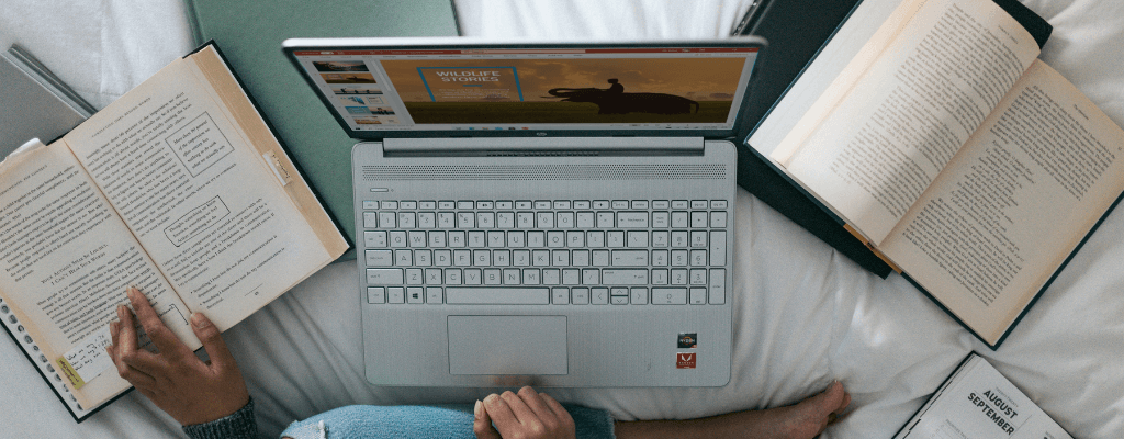 Personne assise avec un ordinateur portable argenté entouré de livres ouverts, vue de dessus