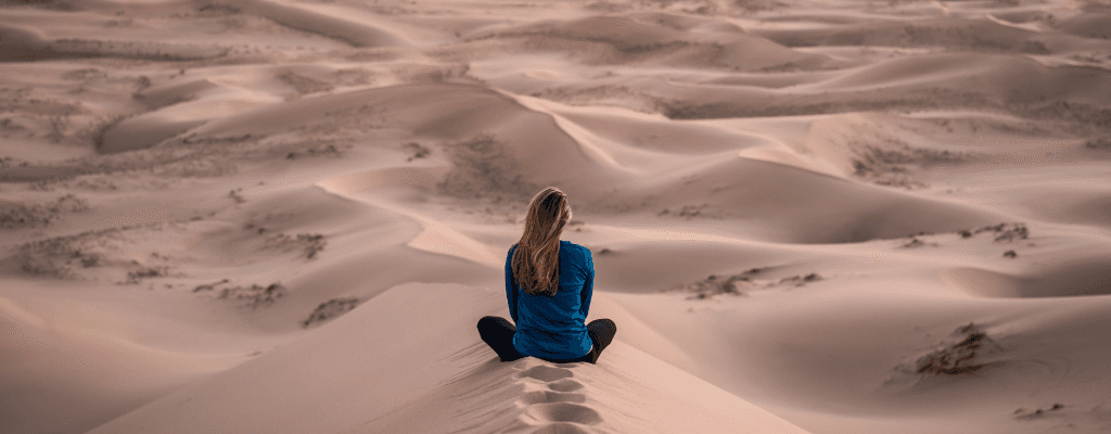 Femme en chemise bleue assise en méditation sur une dune de sable désertique