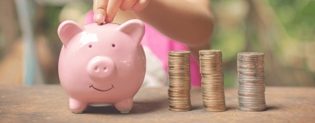 Tirelire cochon rose avec une pièce de monnaie placée dans sa fente, entouré de trois piles de pièces
