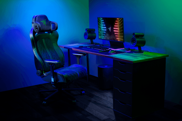 Setup gaming Razer avec fauteuil ergonomique noir et bleu, bureau équipé d'écrans et d'accessoires illuminés aux néons bleu et vert