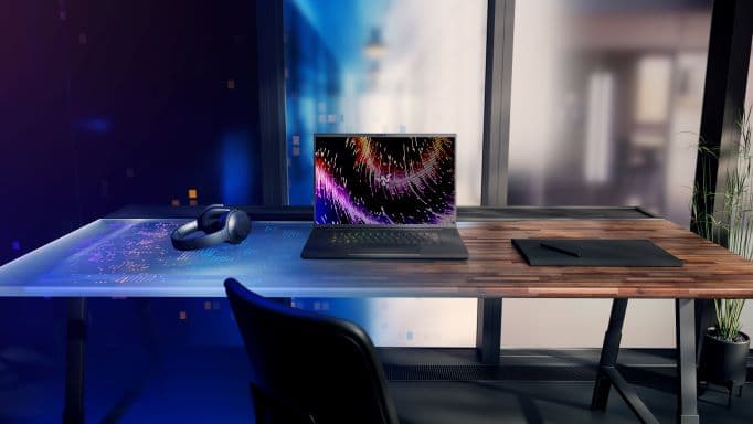 Laptop Razer Blade 16 sur un bureau gaming avec écran affichant des dégradés colorés, casque et souris sans fil à proximité