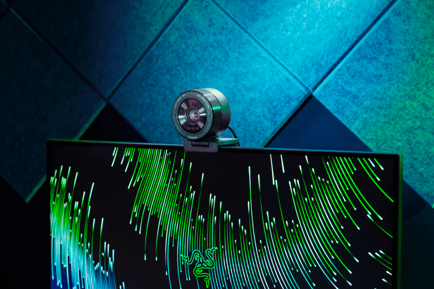 Webcam Razer Kiyo Pro Ultra montée sur un écran affichant des lignes lumineuses vertes et bleues, sur fond turquoise