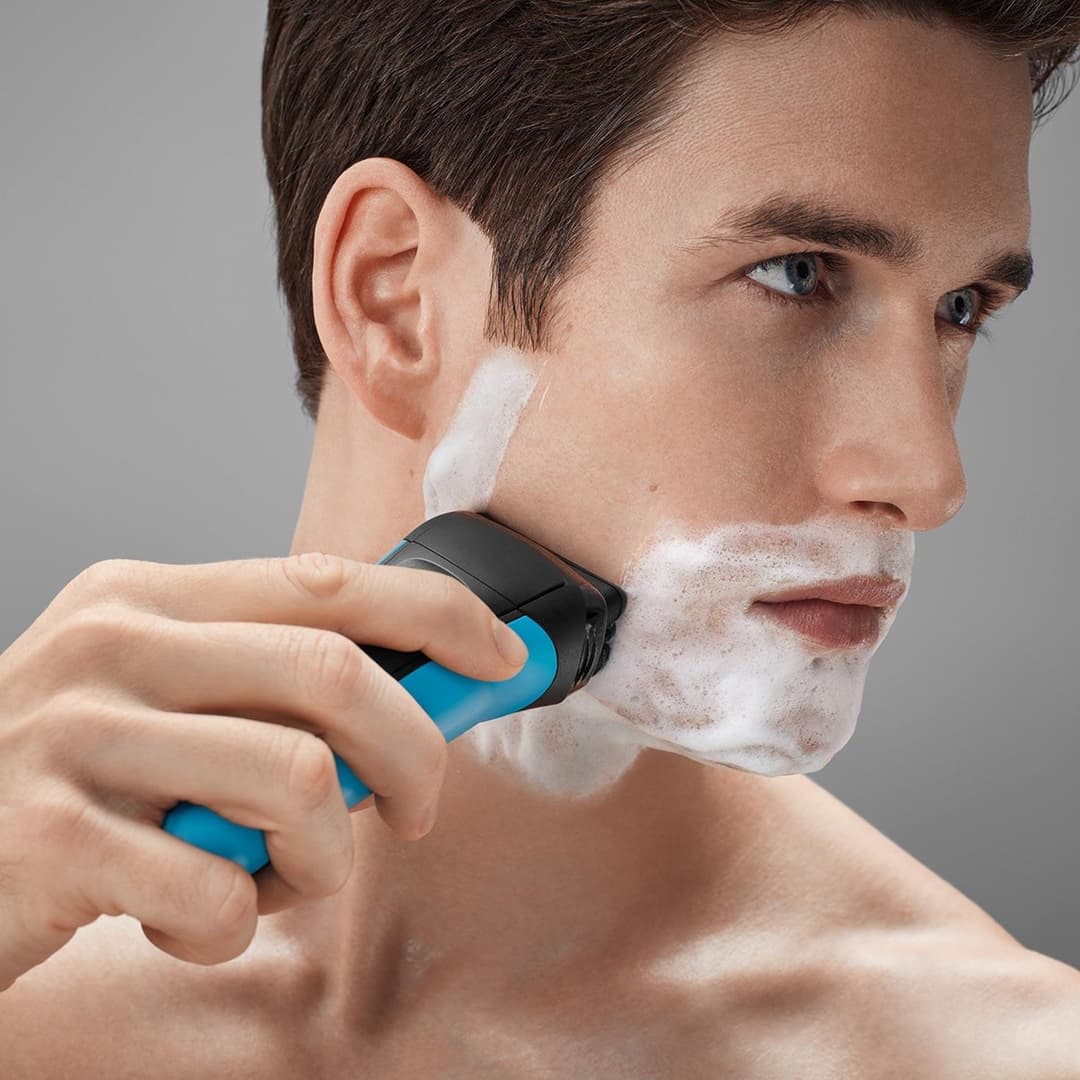 Rasoir électrique Braun Séries 3 noir et bleu utilisé par un homme pour se raser le menton avec de la mousse