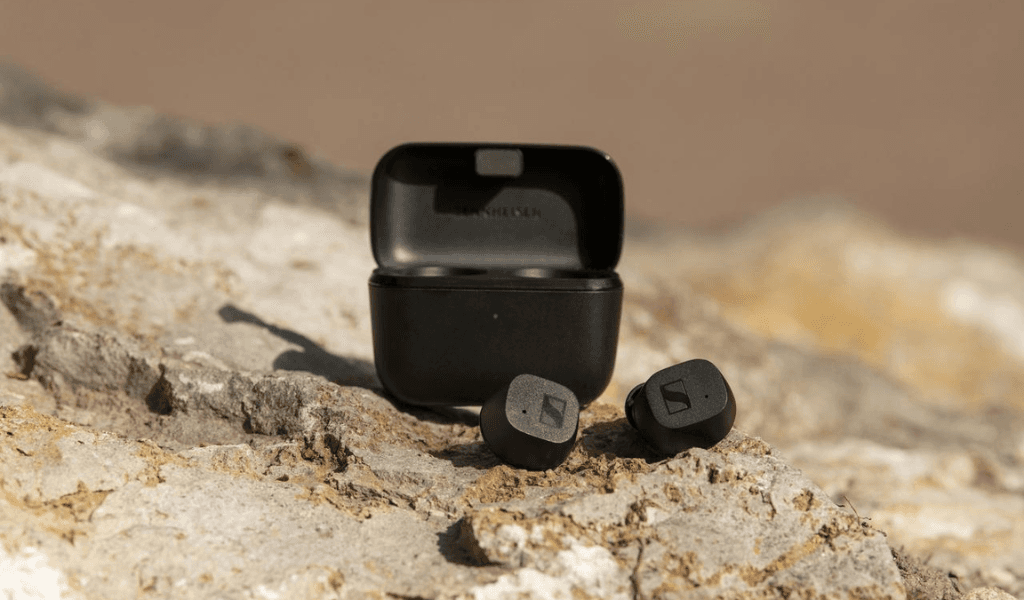 Écouteurs Sennheiser CX True Wireless noirs avec leur boîtier de recharge, posés sur du sable
