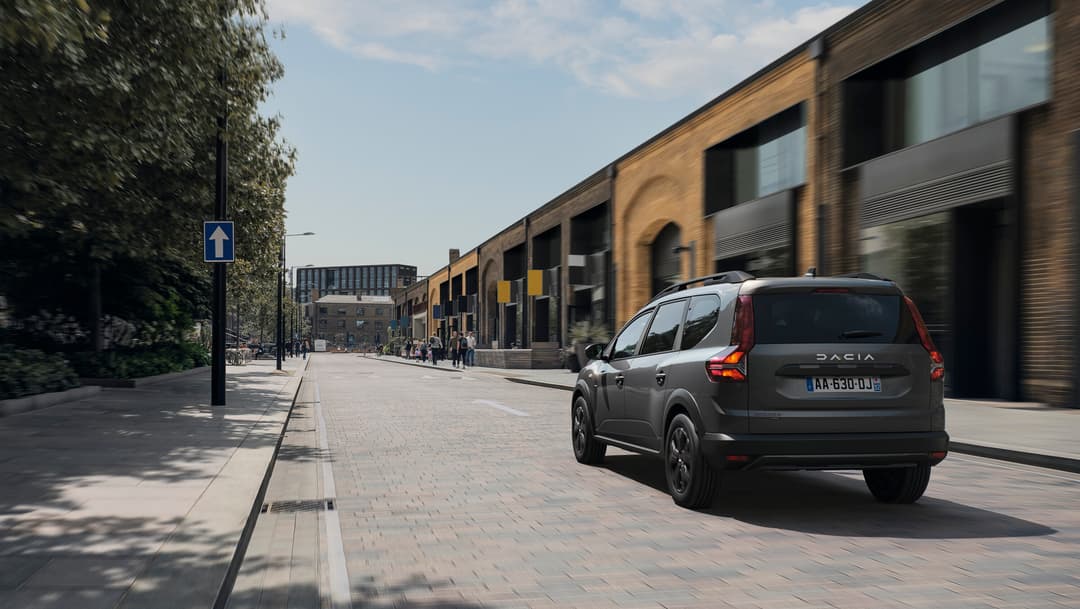 Dacia Jogger Hybrid 140 grise garée dans une rue urbaine, vue de trois quarts arrière
