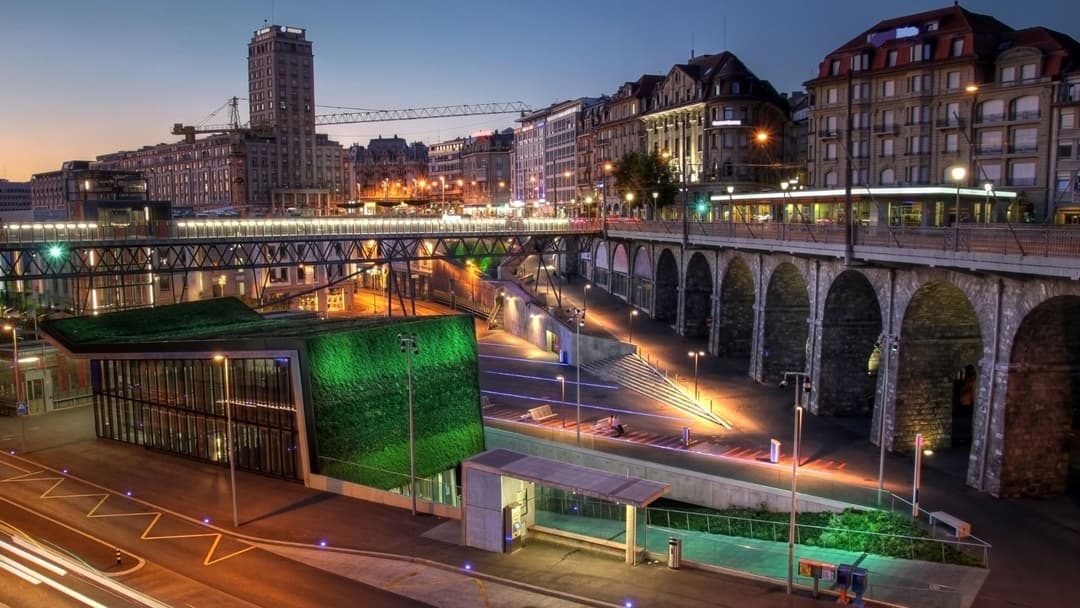 Le Flon à Lausanne de nuit, avec immeubles historiques, viaducs en pierre et bâtiment moderne à façade végétale illuminée de vert