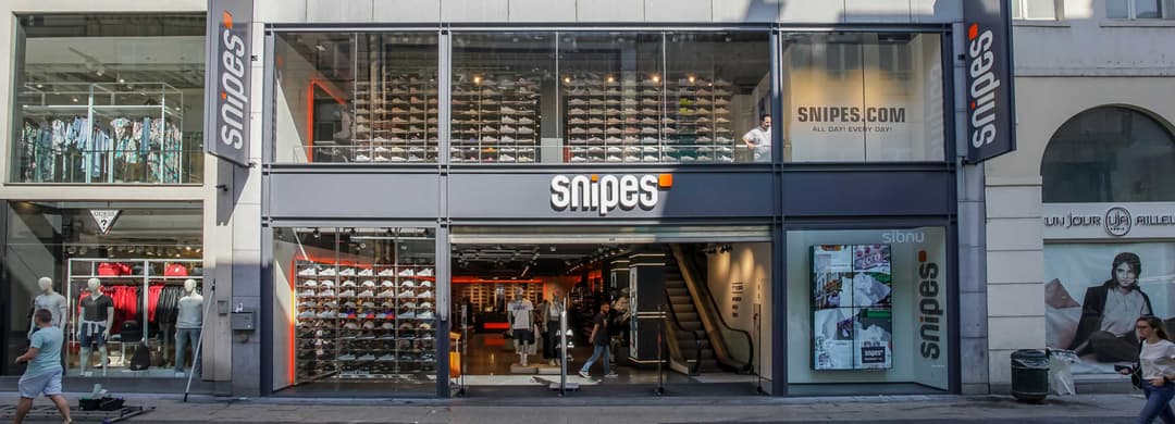 Façade du magasin Snipes avec vitrines exposant des chaussures de sport, enseigne blanche et noire, devanture urbaine animée