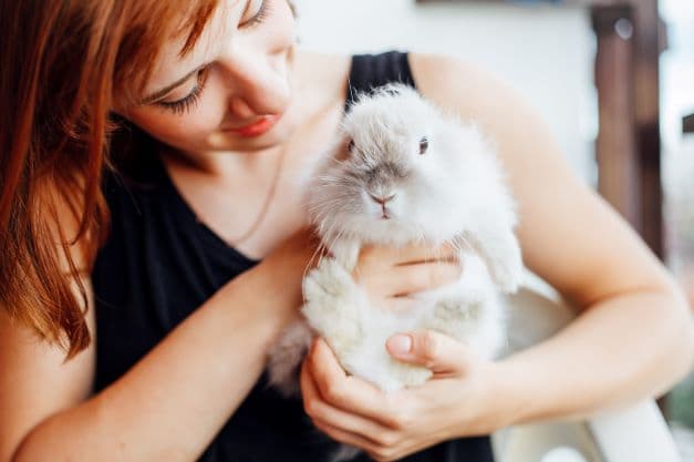 Femme aux cheveux roux tenant un petit lapin blanc dans ses bras, elle le regarde tendrement