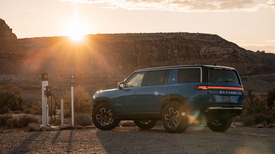 Rivian R1S bleu foncé en charge sur une borne électrique dans un paysage désertique au coucher de soleil