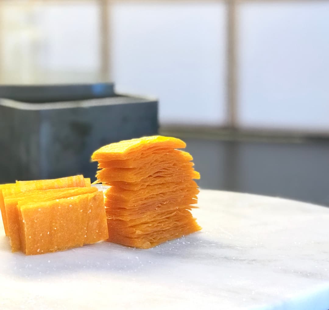 Bonbons orange gélatineux empilés et disposés sur une surface blanche, avec un récipient noir flou en arrière-plan