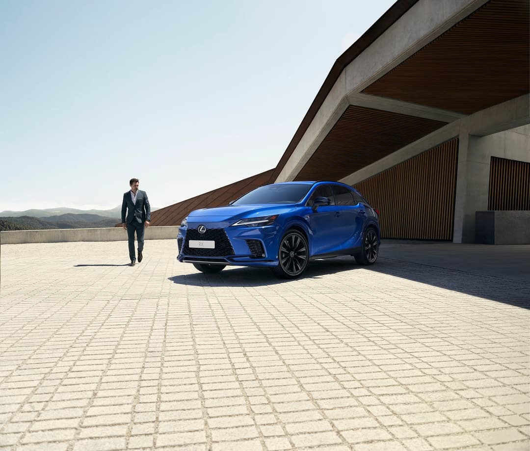 Lexus RX bleu électrique garé devant une structure architecturale moderne, un homme en costume s'en approchant
